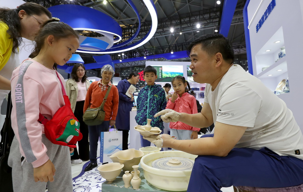 5月12日，江西景德鎮(zhèn)展臺(tái)的工作人員（右）向參觀者介紹瓷器制作的步驟。